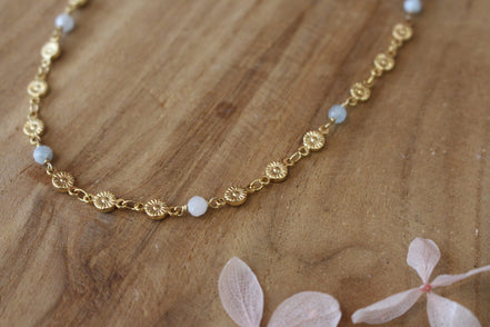collier doré avec des perles facettées en aigue marine, sur une chaine de fleurs dorées